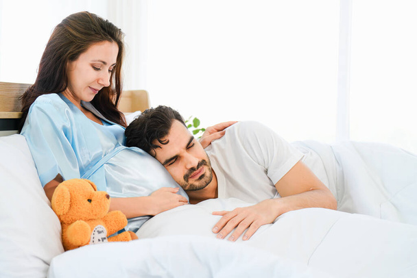 portrait of happy pregnant wife and husband lying together on bed in bed room at home - Foto, Imagen