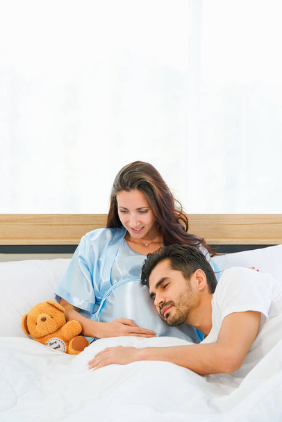 portrait of happy pregnant wife and husband lying together on bed in bed room at home - Foto, Imagen
