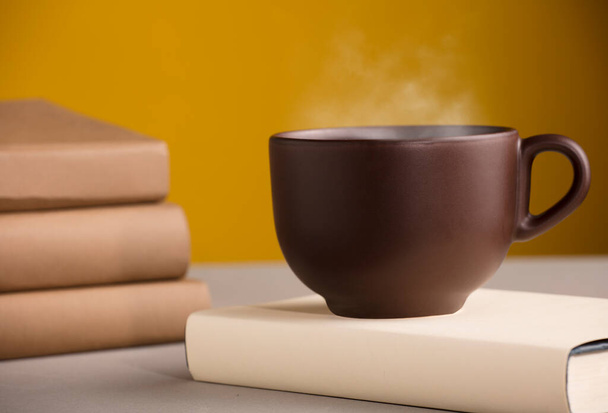 Taza marrón de café o té con vapor caliente, sobre la mesa, con libros - Foto, imagen