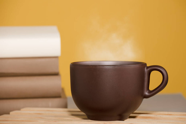 Taza marrón de café o té con vapor caliente, sobre la mesa, con libros - Foto, Imagen