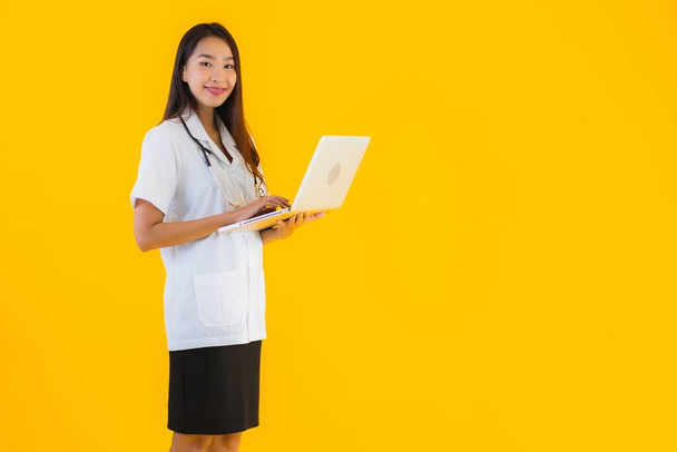 Portré gyönyörű fiatal ázsiai orvos nő használ notebook vagy laptop sárga izolált háttér - Fotó, kép