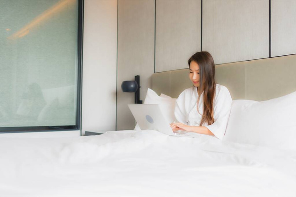 Retrato hermosa joven mujer asiática uso portátil o computadora en el interior del dormitorio
 - Foto, imagen