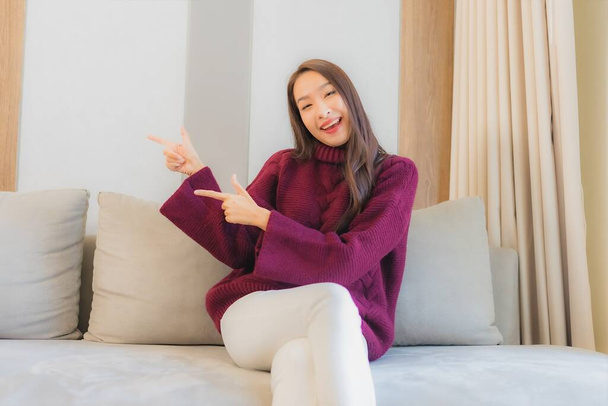 Muotokuva kaunis nuori aasialainen nainen hymy rentoutua sohvalla olohuoneessa sisustus - Valokuva, kuva