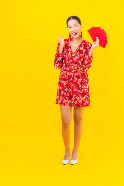 Retrato hermosa joven asiática mujer con sobres rojos sobre fondo amarillo - Foto, imagen