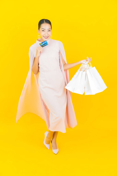 Portré gyönyörű fiatal ázsiai nő hitelkártyával és bevásárló táska sárga színű háttér - Fotó, kép
