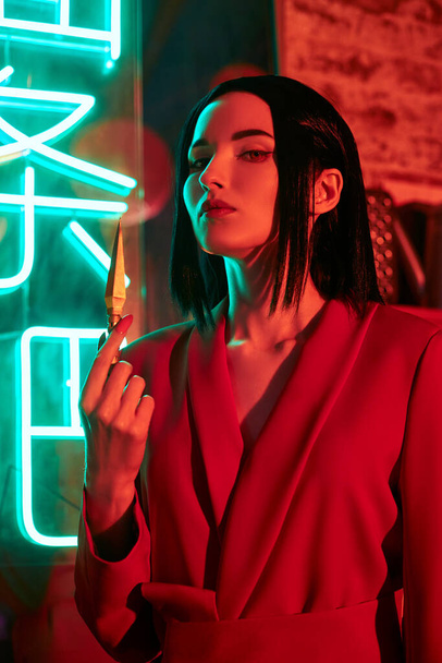 Anime woman in a red suit with short hair cut, black hair. A killer girl in a red jacket with a dagger in her hand. Beauty portrait - Fotografie, Obrázek