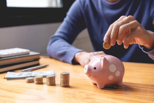 sparen concept de man plukken zijn munt te laten vallen in een roze spaarvarken bank als zijn geld sparen voor deze maand. - Foto, afbeelding