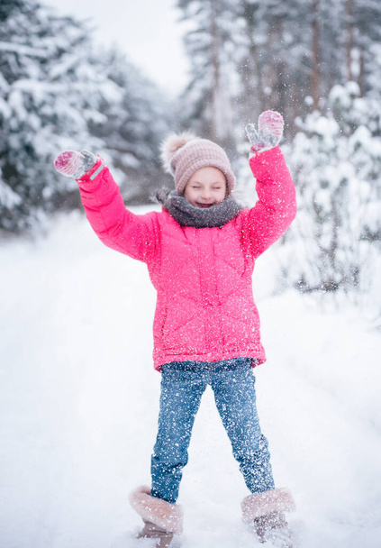 A little girl in a bright jacket plays in the winter snowy forest. - Photo, Image