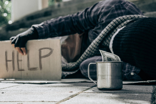 Hombre sin hogar con suéter y manta durmiendo en cartulina buscando ayuda.Pobre hombre sin hogar y concepto de depresión. - Foto, Imagen