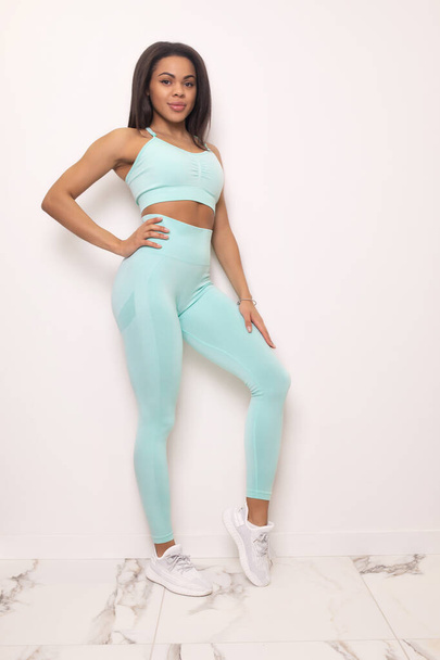 full length view of young fit african american woman in sportswear smiling at camera and posing in studio - Photo, image