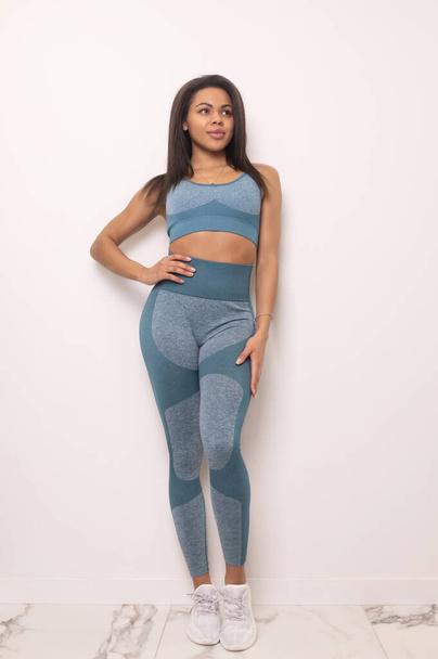 full length view of smiling young fit african american woman in blue sportswear posing in studio - 写真・画像