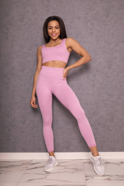 beautiful young fit woman in pink sportswear smiling at camera and posing in studio - Fotó, kép