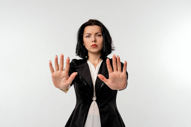 Seriöse junge Geschäftsfrau in schwarzer Jacke und weißem Hemd mit Stopp-Geste und vereinzelten Handflächen auf schwarzem Hintergrund. Soziale Distanzierung. Neues normales Verhalten. Geschäftskonzept - Foto, Bild