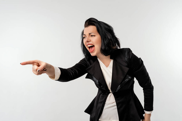 Siyah resmi ceketli iş kadını beyaz gömlekli kızgın agresif bir ifadeyle yanal fotokopi alanını gösteriyor öfkeli, çılgın bir patron gibi görünüyor, beyaz arkaplanı izole ediyor. İş konsepti - Fotoğraf, Görsel