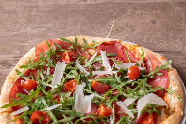 close up of delicious italian fresh pizza with ham, arugula, tomato and parmesan - Photo, Image