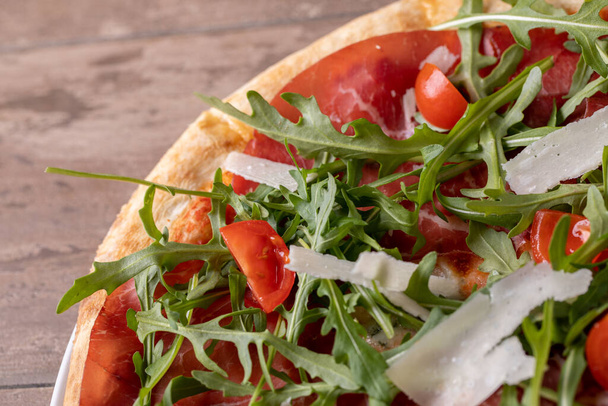 primer plano de deliciosa pizza fresca italiana con jamón, rúcula, tomate y parmesano - Foto, imagen