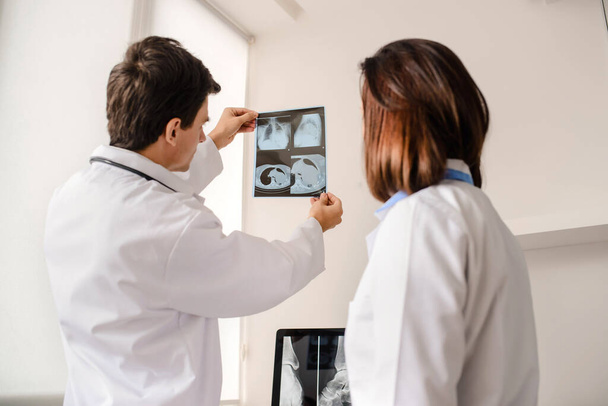 In de medische ruimte twee jonge artsen radiologen analyseren x-ray en computer tomografie film en maak een medische beschrijving in notebook - Foto, afbeelding