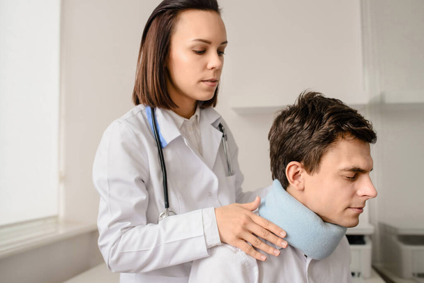 Jonge vrouw arts toe te passen traumatologische kraag op een mannelijke patiënt die nek probleem - Foto, afbeelding