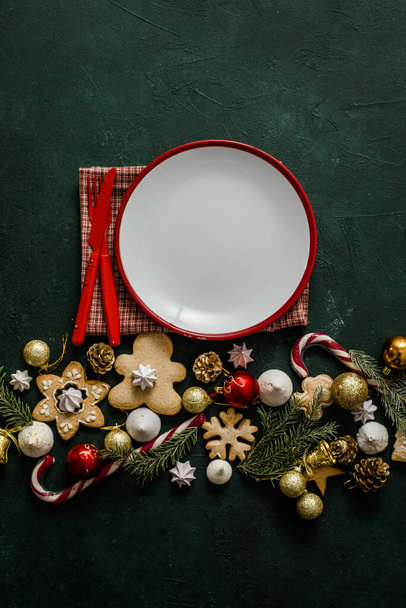 Kerstmis en Nieuwjaar tafel dekken. Wit leeg bord met bestek en kerstboomtakken, rood servet op een rode betonnen ondergrond. - Foto, afbeelding