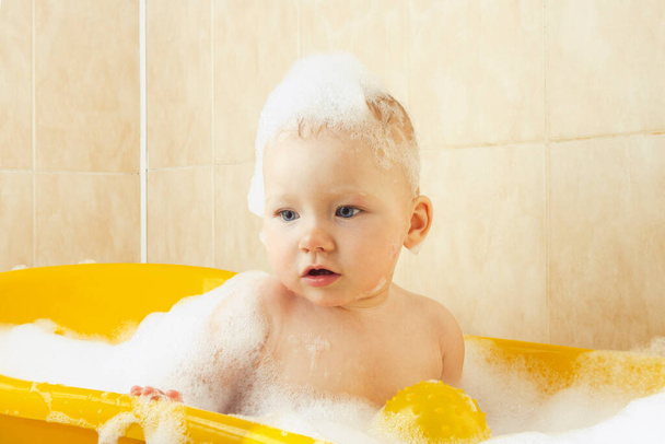 Petit bébé prend un bain dans un bain jaune avec des bulles et de la mousse. Le concept d'enfant heureux, l'amour pour le bain - Photo, image