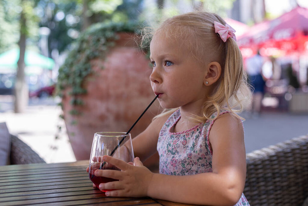 Παιδί πίνει ένα ποτό στην καλοκαιρινή βεράντα κάτω από φυσικό φως. Πραγματικοί άνθρωποι. - Φωτογραφία, εικόνα