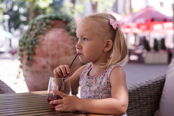 Child drinking a drink on the summer terrace under natural light. Real people. - Foto, imagen