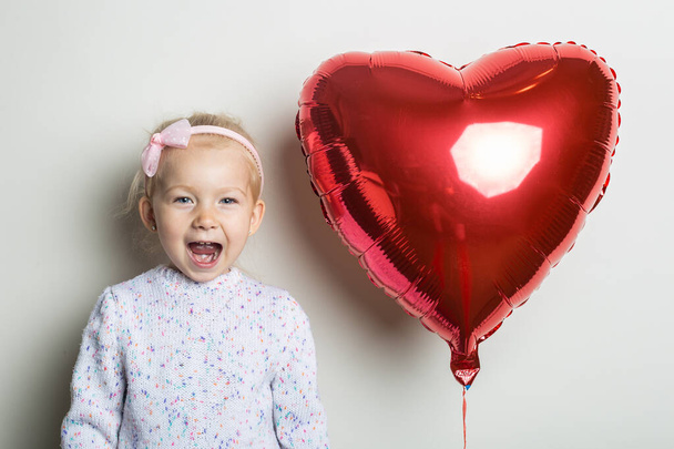 Surprised little girl and heart air balloon on a light background. Concept for Valentine's Day, birthday. Banner. - Photo, Image