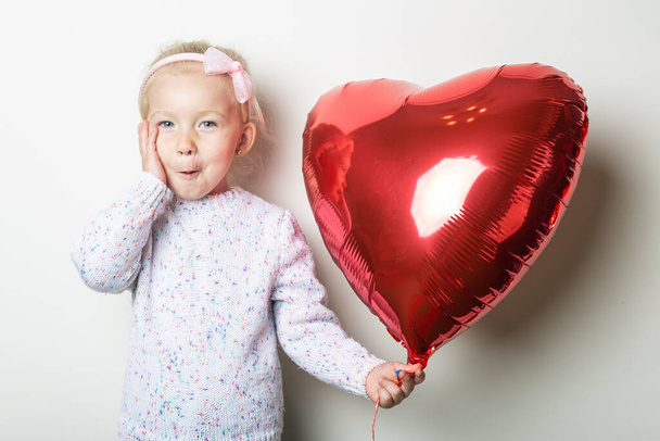 Удивлённая маленькая девочка, держащая воздушный шар на светлом фоне. Концепция на День Святого Валентина, день рождения. Баннер. - Фото, изображение