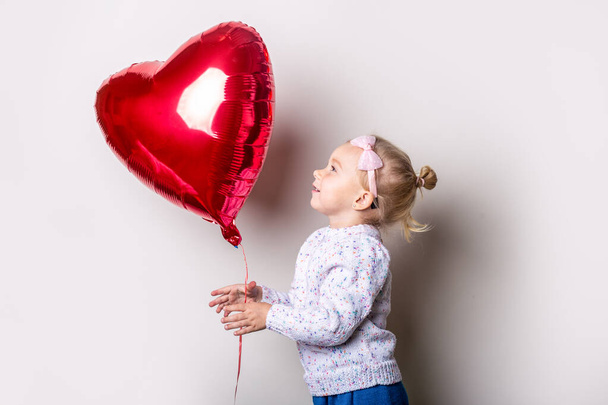 Little girl catches a heart air balloon on a light background. Concept for Valentine's Day, birthday. Banner. - Foto, Imagem