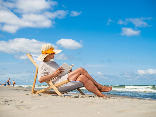 Woman relaxing on beach reading book sitting on sunbed  - Foto, Imagem