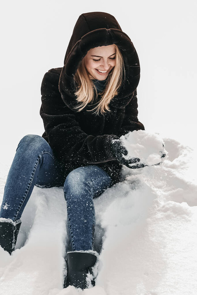 Woman is sitting in the snow and playing with it. - Foto, Bild
