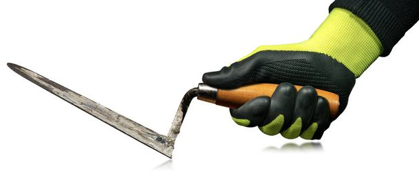 Manual worker with protective work gloves holding a dirty trowel with a wooden handle. Isolated on white background, photography. - Photo, Image
