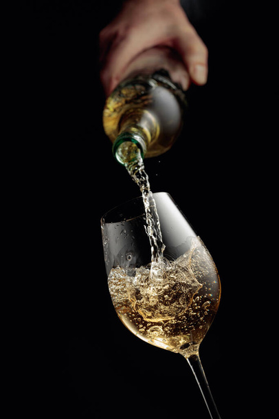 Pouring white wine in a glass goblet. Black background with copy space. - 写真・画像
