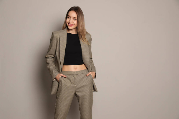 Portrait of beautiful young woman in fashionable suit on grey background, space for text. Business attire - Φωτογραφία, εικόνα