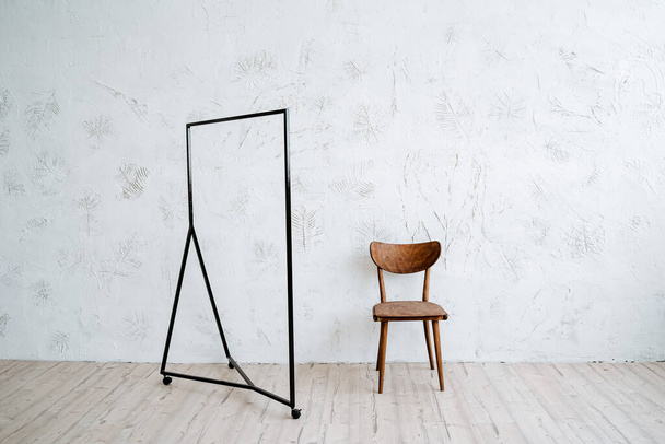 Metal hanger floor on a minimalist background. Rack for clothes on wheels. Nearby is a vintage wooden chair. Light walls, wooden floor in the room. High quality photo - Foto, Bild