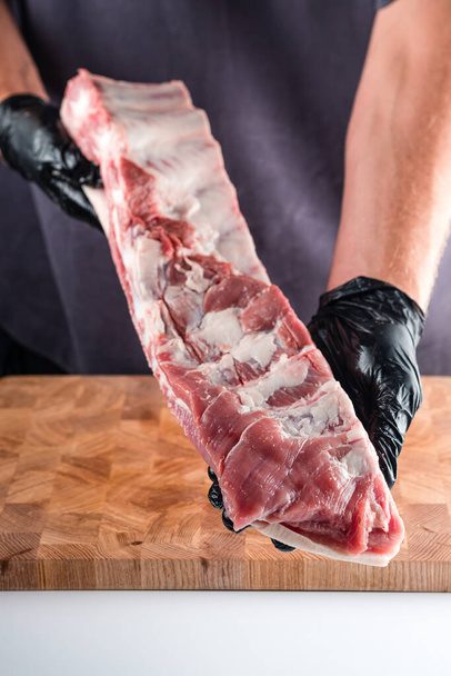 rauwe varkensribbetjes in de handen van een slager, varkensbuik boerderij vers varkensvlees buik slager die spek porchetta - Foto, afbeelding
