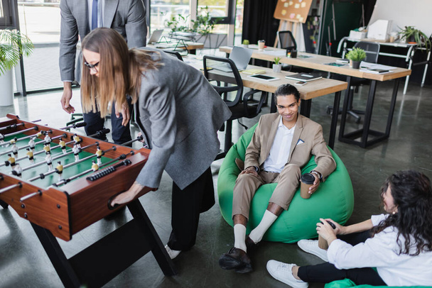 interracial business people sitting in bag chairs near colleagues playing table football in office - Foto, immagini
