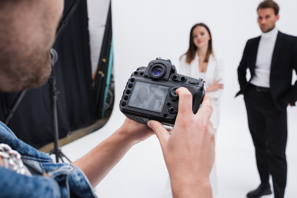 fotógrafo profesional mirando el visor de la cámara digital cerca de modelos borrosas en el estudio de fotografía - Foto, Imagen