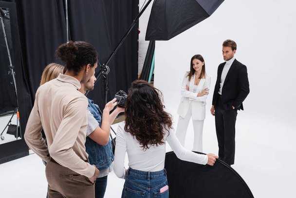 fotógrafo con colegas multiétnicos mirando la cámara digital cerca de modelos jóvenes y de moda - Foto, Imagen
