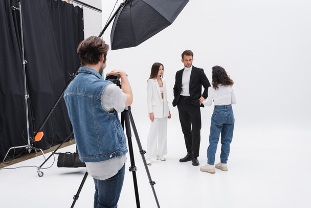 photographer adjusting digital camera while art director talking with models in photo studio - Foto, afbeelding