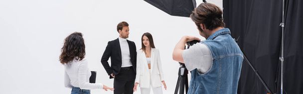 director creativo hablando con modelos con estilo cerca de fotógrafo que trabaja en el estudio de fotografía, pancarta - Foto, Imagen