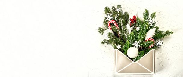Christmas festive composition with fir tree branches, New Year toys, snowflakes, and traditional decoration. Envelope, white background, creative flat lay, banner format - 写真・画像