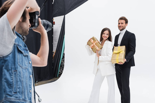 fotógrafo borroso tomando fotos de modelos sonrientes con cajas de regalo en blanco - Foto, Imagen
