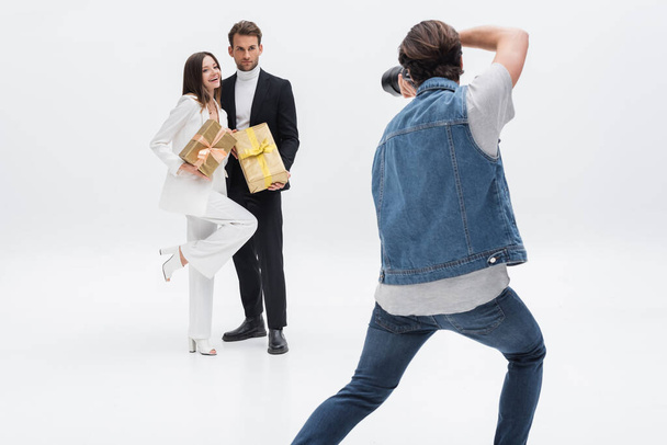 back view of professional photographer taking picture of trendy models with gift boxes on white - Фото, изображение