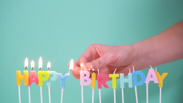 Happy Birthday concept Made of Burning Colorful Candles on blue or turquoise background. Hand lights candles words Happy birthday. 4K resolution video - Footage, Video