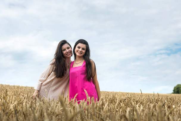 Buğday tarlasında güzellik kıyafeti giymiş iki kadın, yaz günü. - Fotoğraf, Görsel