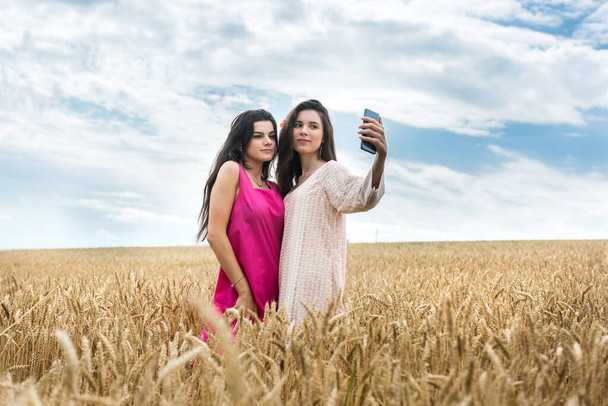 twee vrouwen in schoonheid jurk possing op tarweveld, zomerdag - Foto, afbeelding