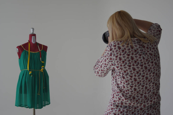 A photographer female taking pictures of the tailor's mannequin with a green dress - Valokuva, kuva