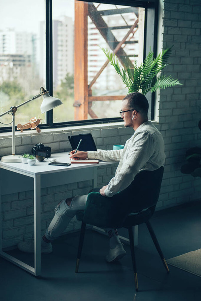 Taustakuva valkoihoisesta miehestä, joka kirjoittaa päiväkirjaansa työpöydän ääreen kannettavan tietokoneen avulla. Suunnittelijan käsite - Valokuva, kuva