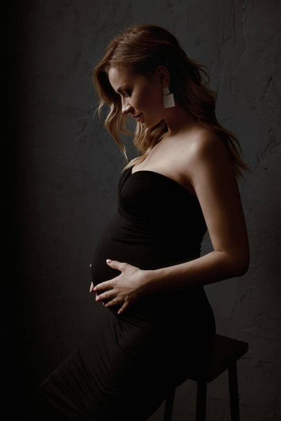 Young pregnant woman with long blond hair holding her belly and looking at it - Foto, afbeelding